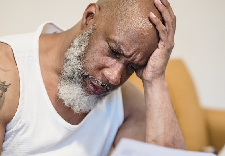 Man in white top looks concerned while reading a document, illustrating stress or focus in decision-making process