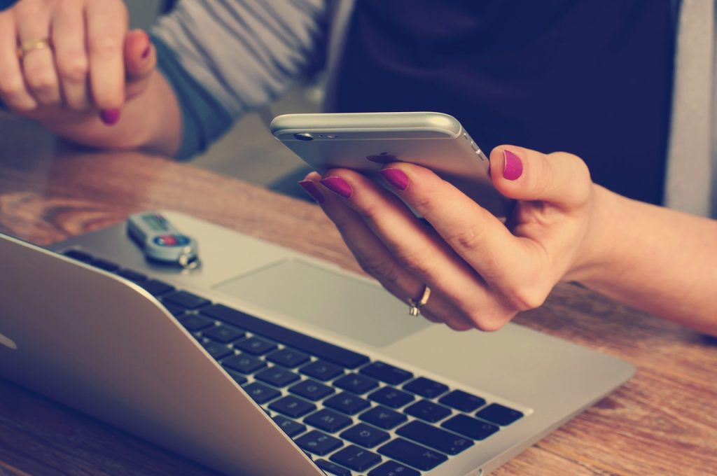 A woman using a laptop while holding a cell phone, engaged in multitasking with technology